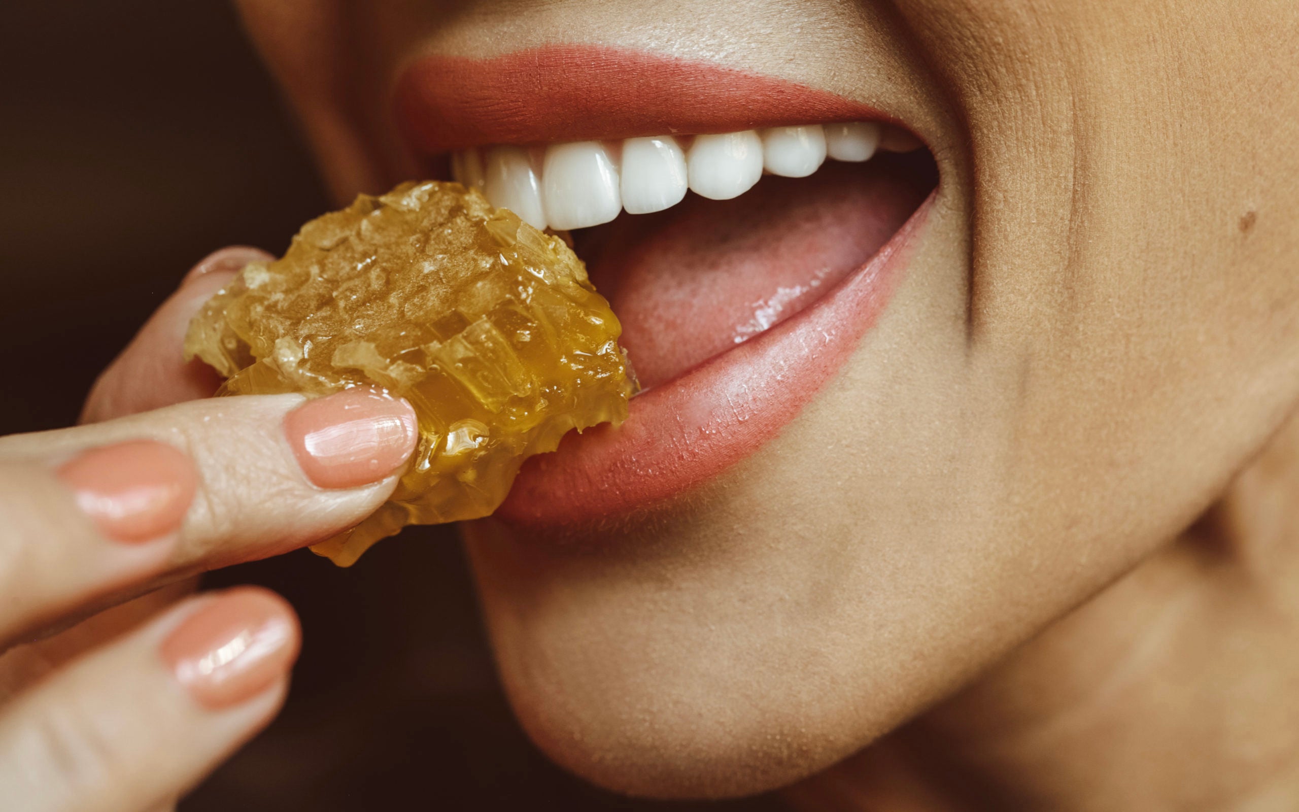 image of a woman biting a piece of portioned unadulterated honeycomb - pass the honey